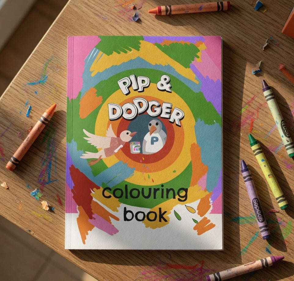Coloring book titled 'Pip & Dodger' on a wooden table with crayons around it.
